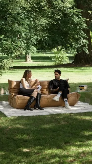 The sofa and rug set up on grass in a park.